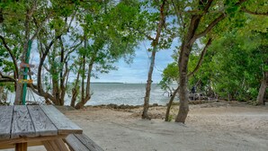 Une table de pique-nique en bois avec un panneau indicateur, le tout situé sur une plage.