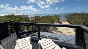 Une terrasse en bois avec des chaises blanches, donnant sur une plage et l’océan.