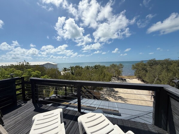 A wooden deck with white chairs, overlooking a beach and ocean.