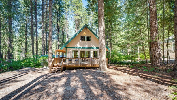 A cabin with a wooden deck and a covered porch, surrounded by tall trees. - Peaceful Leavenworth Cabin with Deck & Fire Pit! (Leavenworth)
