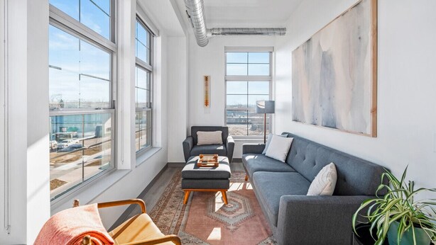 A modern living room with large windows, a grey sofa, a black armchair, and a coffee table. - Oak Tree House 305 (Traverse City)