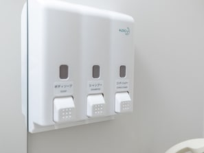 Un distributeur mural doté de trois compartiments étiquetés « savon », « shampoing » et « après-shampoing ».