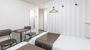 Habitación de hotel con dos camas, un escritorio, una silla, un espejo, un perchero y un termostato.