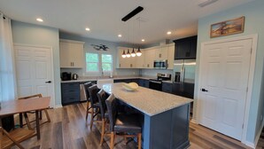 A modern kitchen with a central island, dark cabinetry, and a dining area with a wooden table and chairs. - New modern home, 3 minute walk to the beach, on bike trail, full RV hookup (Panacea)