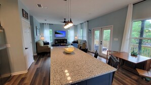 A modern kitchen with a granite countertop, a built-in island, and a dining area with a wooden table and chairs. - New modern home, 3 minute walk to the beach, on bike trail, full RV hookup (Panacea)