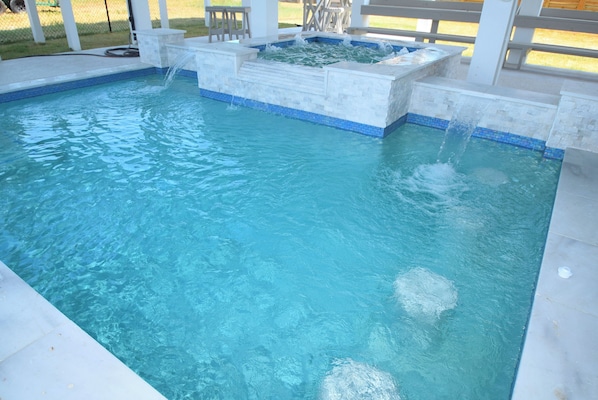 Une piscine à l’eau d’un bleu cristallin, un jacuzzi intégré et des marches menant à l’intérieur de la piscine.