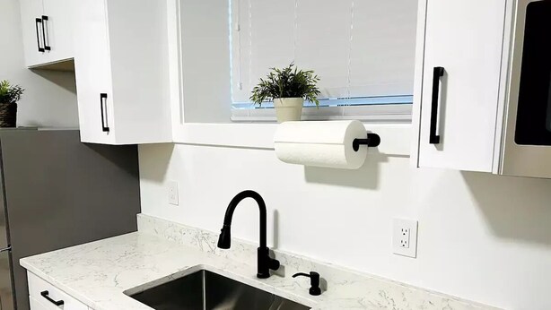 A kitchen with a stainless steel sink, white cabinets, a black faucet, and a window with blinds.