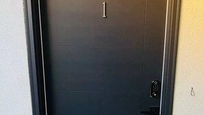 A dark-colored door with a number '1' above it, a keypad lock, and a doormat with 'WELCOME TO OUR HOME' written on it.