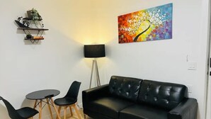 A living room with a black leather sofa, two black chairs, a small round table, a floor lamp, and a colorful abstract painting on the wall.