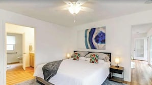 Une chambre à coucher avec un lit, des tables de chevet, un ventilateur de plafond et un tableau accroché au mur.