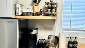 Una cocina moderna con un refrigerador de acero inoxidable, una cafetera, un tostador, un hervidor y frascos de especias sobre una encimera de madera.