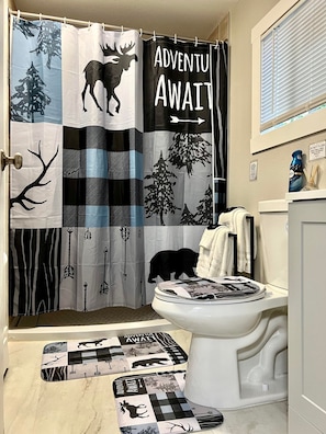 A bathroom with a shower curtain featuring a wildlife theme, a toilet, and a magazine rack. - Log cabin in heart of Anchorage (Anchorage)