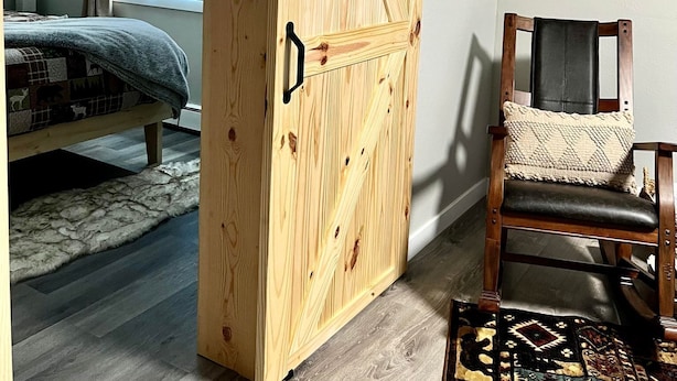 Un dormitorio con un armario de madera, una cama, una silla y una ventana con cortinas.