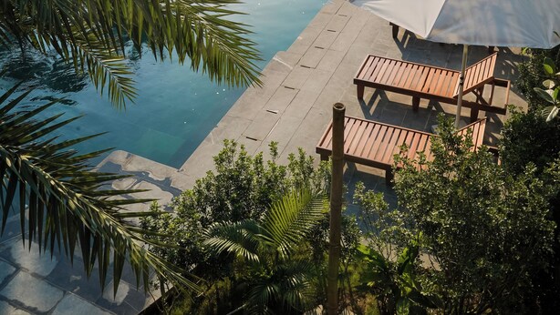 A pool area with lounge chairs and umbrellas, surrounded by lush greenery and mountains in the background. - Tam Coc Retreat Ninh Bình (Nam Hoa Lu)