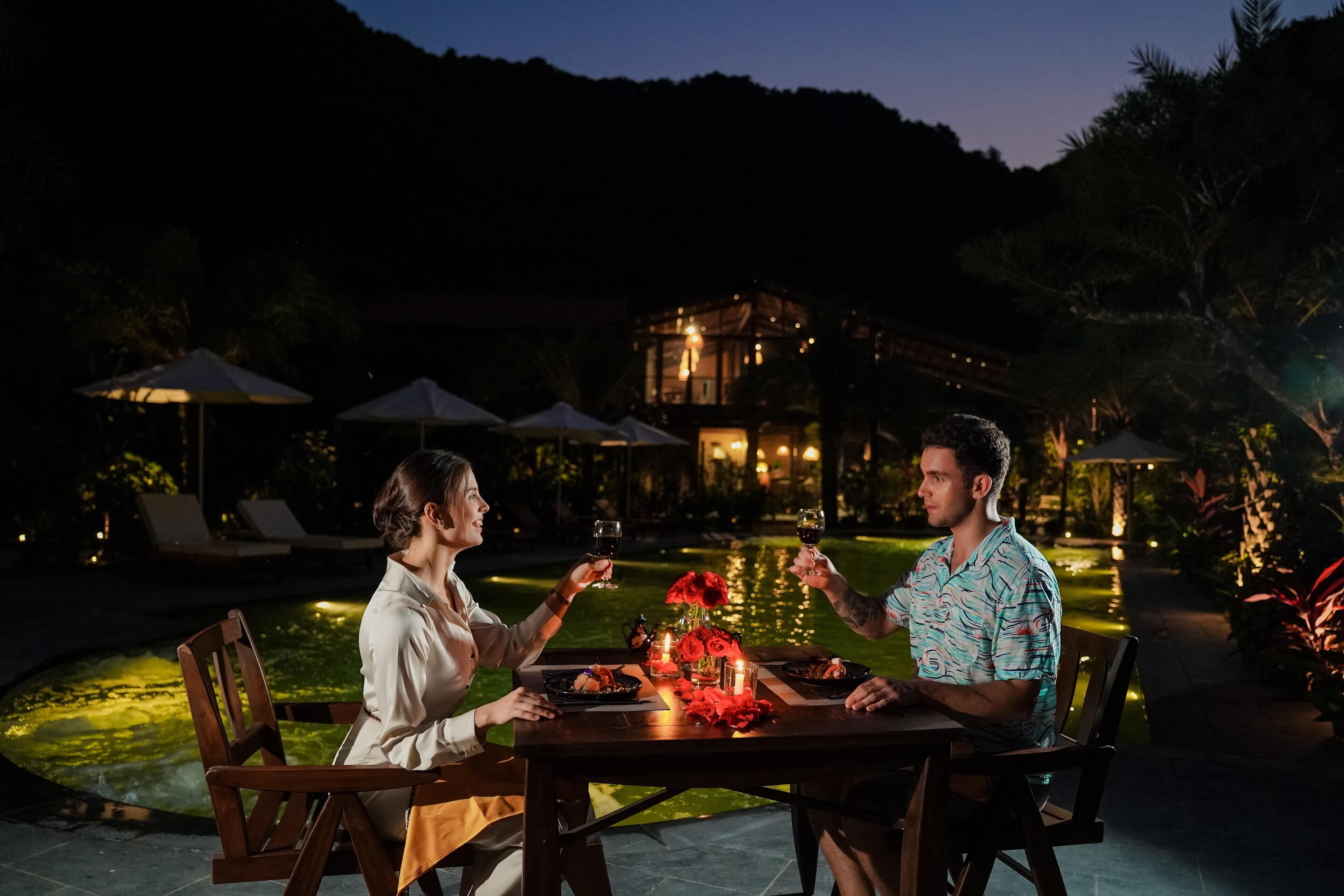 A couple dining at an outdoor table with a view of a pool and a building in the background.