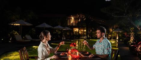 A couple dining at an outdoor table with a view of a pool and a building in the background.