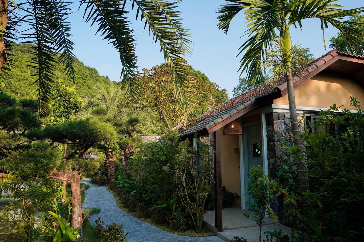 Un chemin menant à un bâtiment entouré d’une végétation luxuriante et de palmiers.