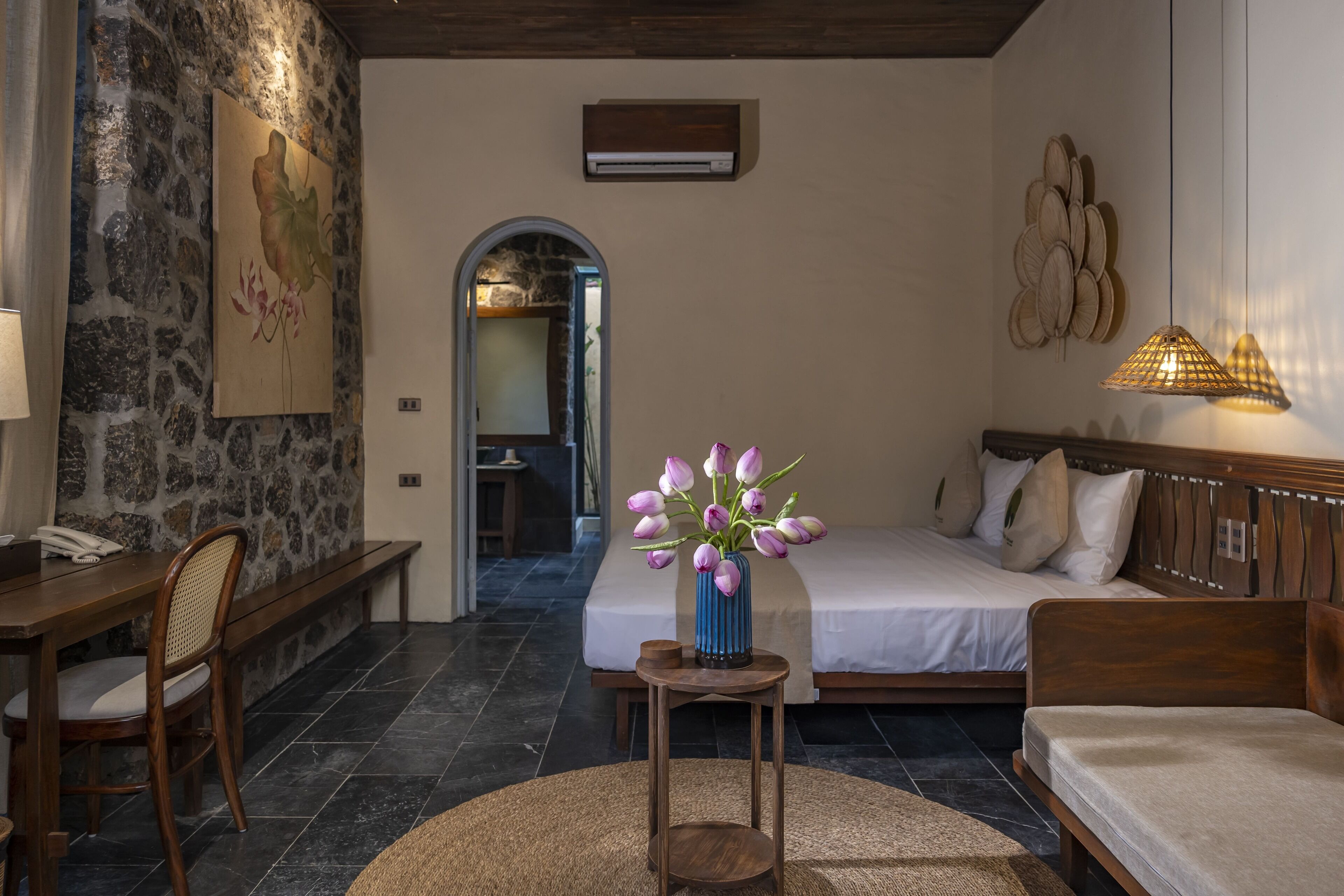 Ein Schlafzimmer mit Bett, Nachttisch und einem kleinen runden Tisch mit Blumen in einer Vase.