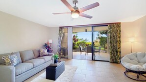 Un salon moderne avec un canapé gris, une table basse, un ventilateur de plafond et une porte-fenêtre coulissante donnant sur une terrasse ext érieure.