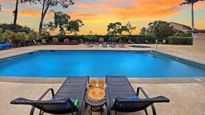 Un espace piscine avec des chaises longues et une table, entouré d’arbres et offrant une vue sur le coucher de soleil.