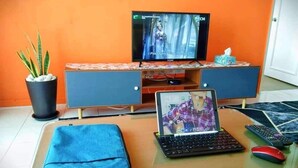 Habitació amb televisió, portàtil, comandament a distància i ratolí sobre una taula.