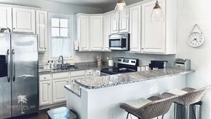 A modern kitchen with white cabinets, stainless steel appliances, a granite countertop, and a bar area with wicker chairs. - Stunning and Clean Hidden Gem w/ 2 Pools Beach Golf & Shops in Barefoot (North Myrtle Beach)