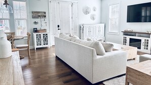 A living room with a sofa, wooden flooring, white walls, and a ceiling fan. - Stunning and Clean Hidden Gem w/ 2 Pools Beach Golf & Shops in Barefoot (North Myrtle Beach)