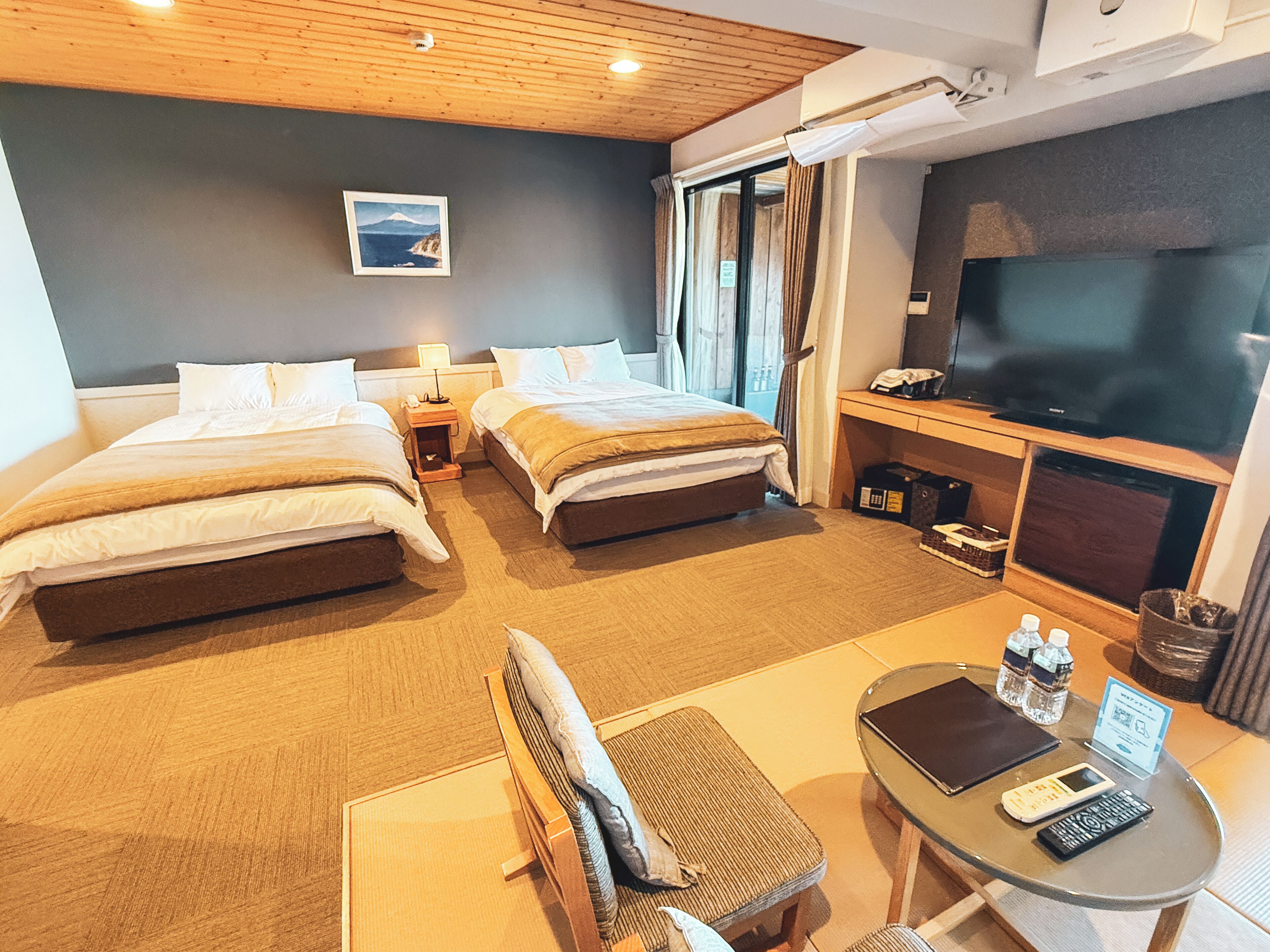 A hotel room with two beds, a TV, a desk with a chair, and a window with curtains.