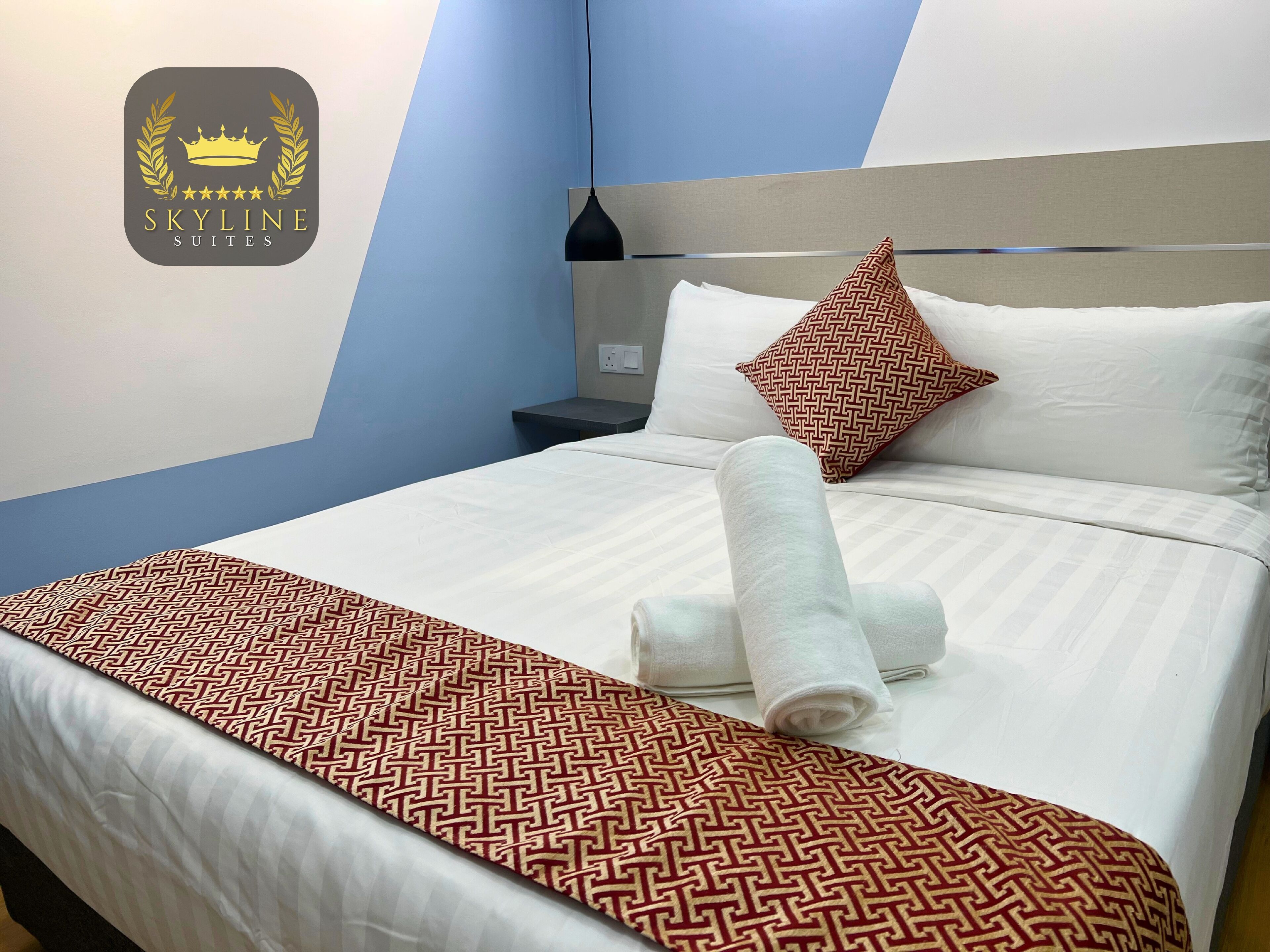 Habitación de hotel con cama, mesita de noche, lámpara y almohada con diseño geométrico.