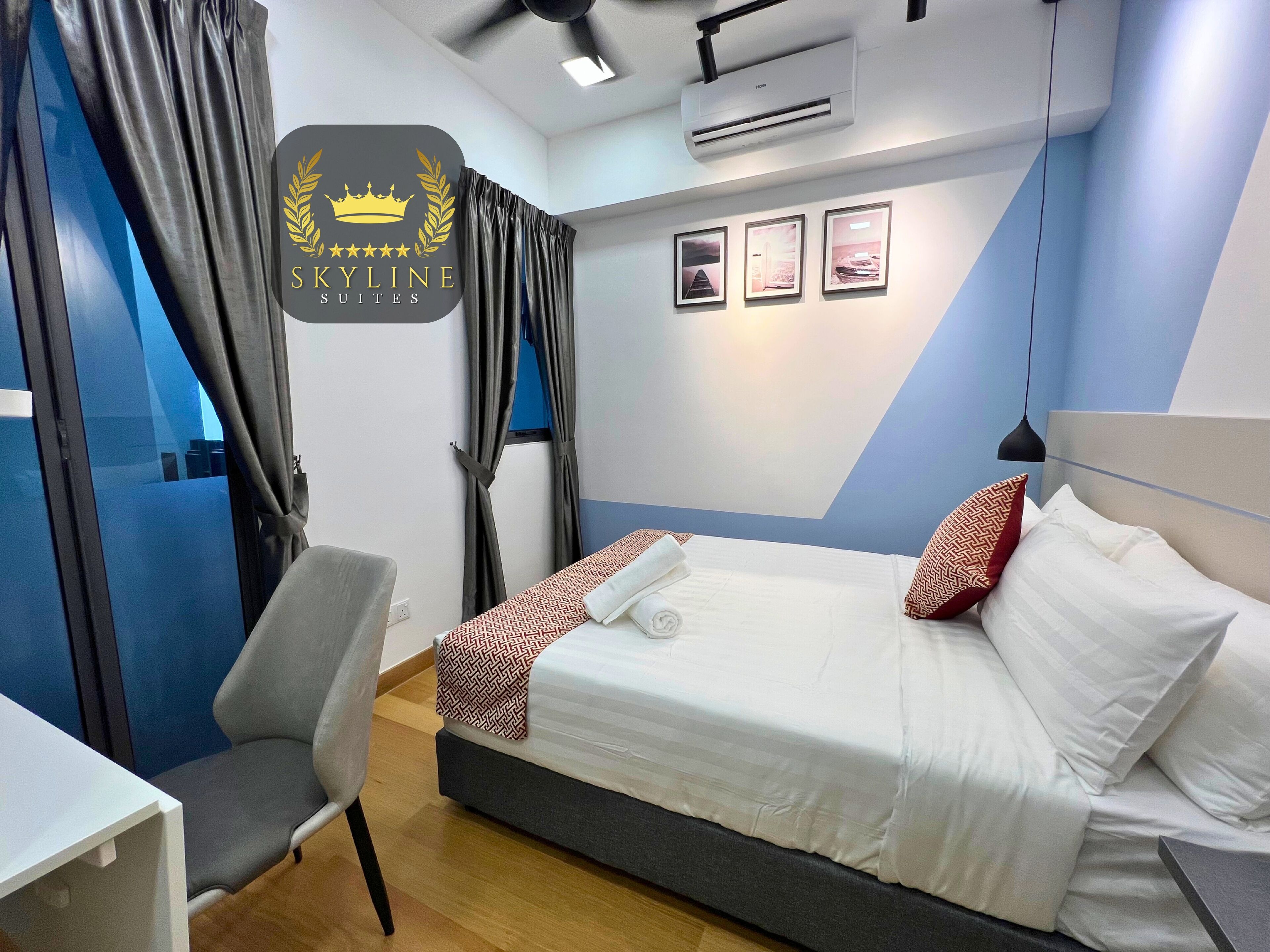 A hotel room with a bed, a desk, and a chair. There is an air conditioning unit on the wall and a ceiling fan.