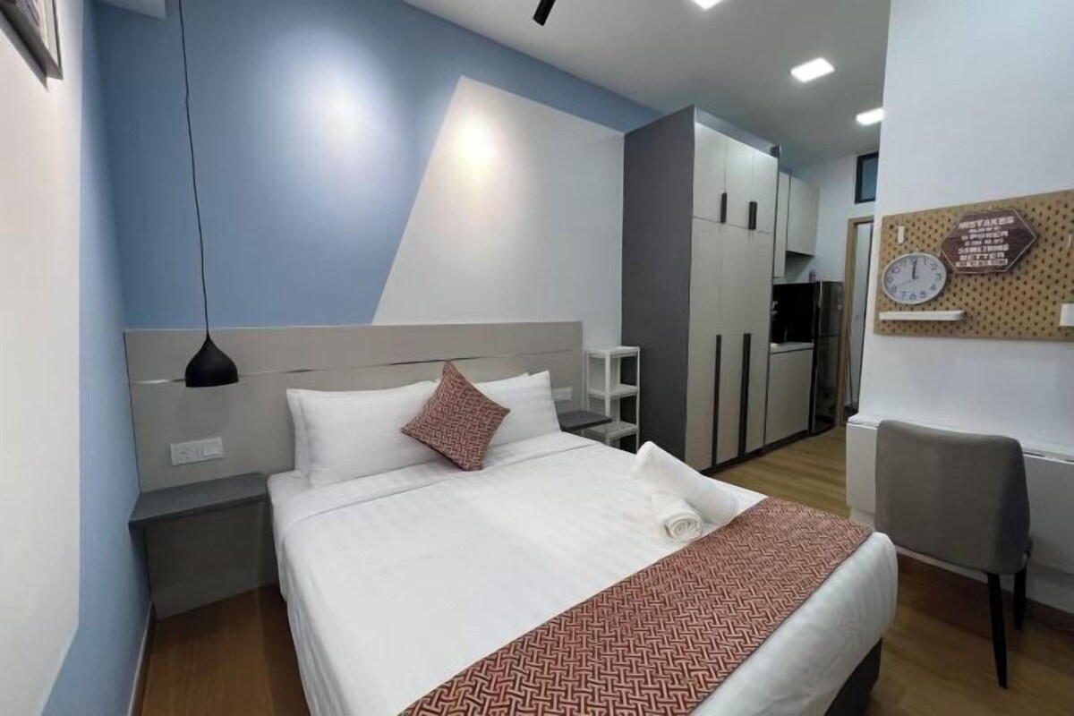 A hotel room with a bed, a desk, a chair, a wardrobe, and a kitchen area.