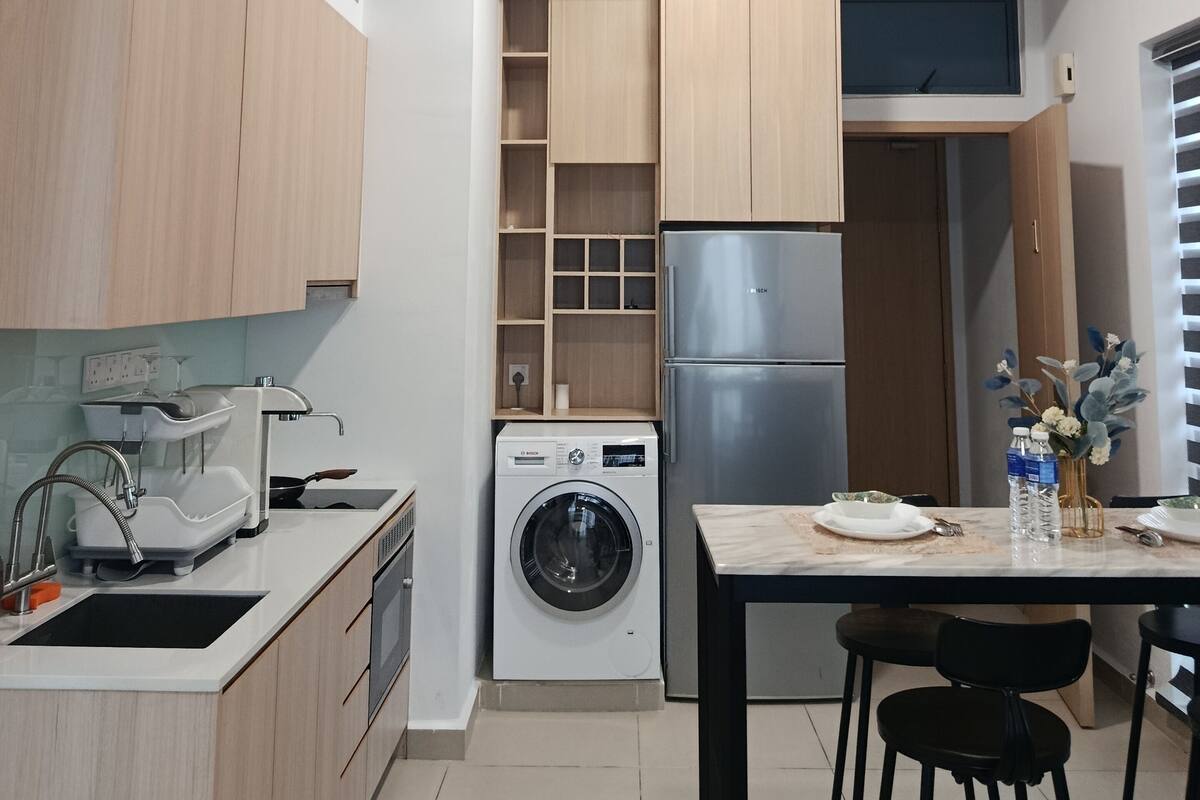Une cuisine moderne avec des meubles en bois, un lave-linge encastré, un réfrigérateur en acier inoxydable et un ventilateur de plafond.