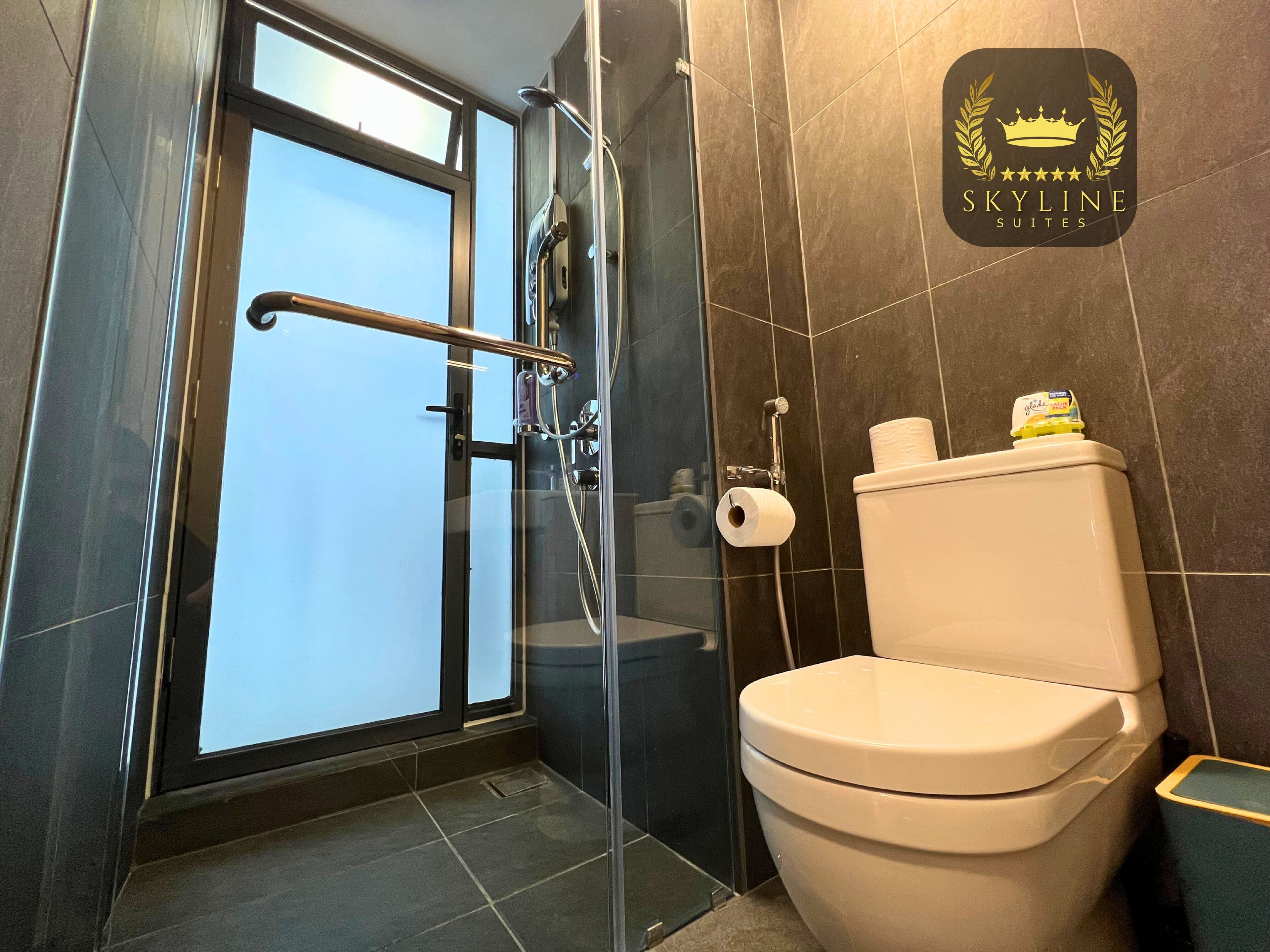 Un baño con cabina de ducha de vidrio, inodoro y un dispensador de papel higiénico a la vista.