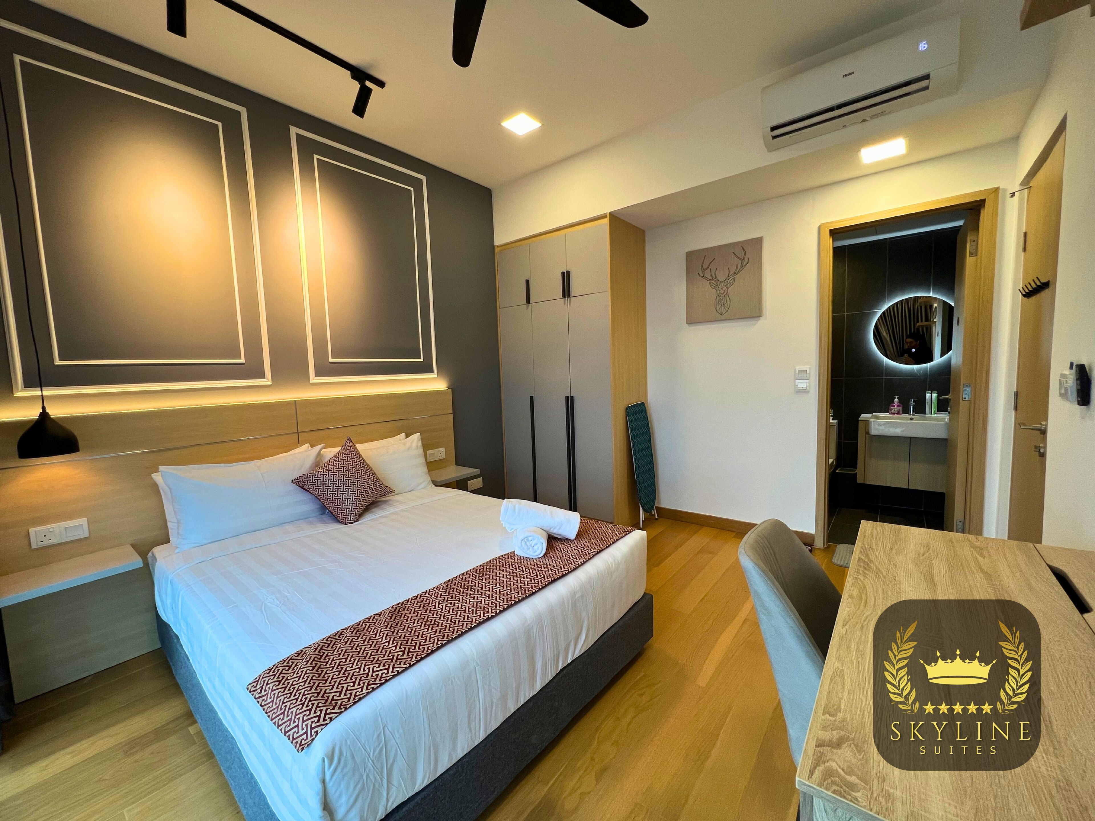 Une chambre d’hôtel moderne, avec un lit soigneusement fait, un bureau en bois et une salle de bain visible à travers une porte ouverte.