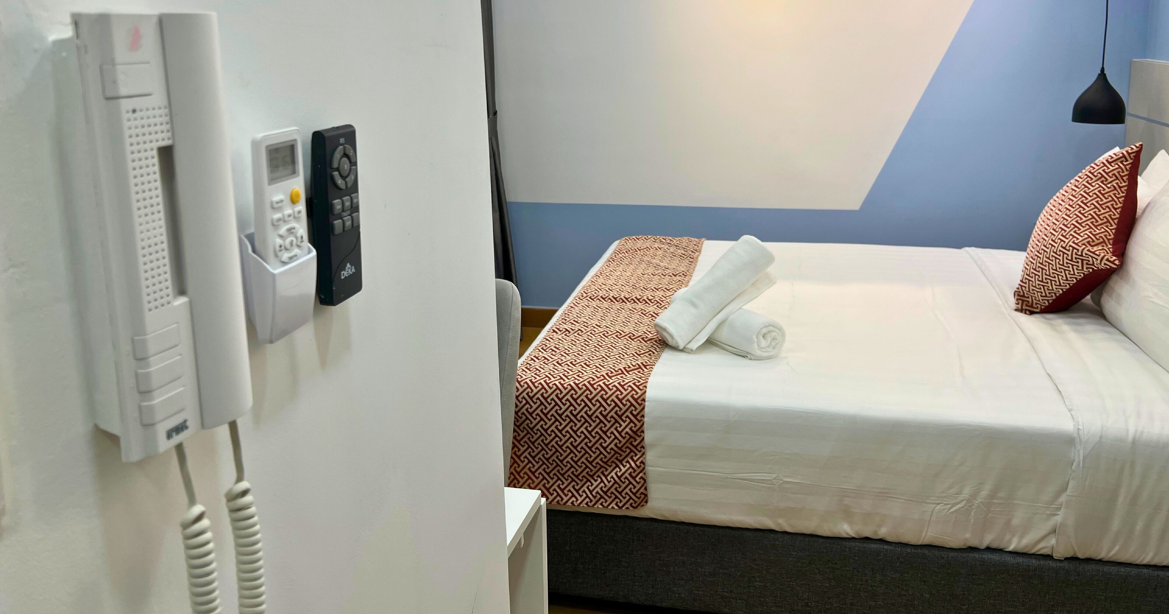 Habitació d'hotel amb un llit, un telèfon i un panell de control fixat a la paret.