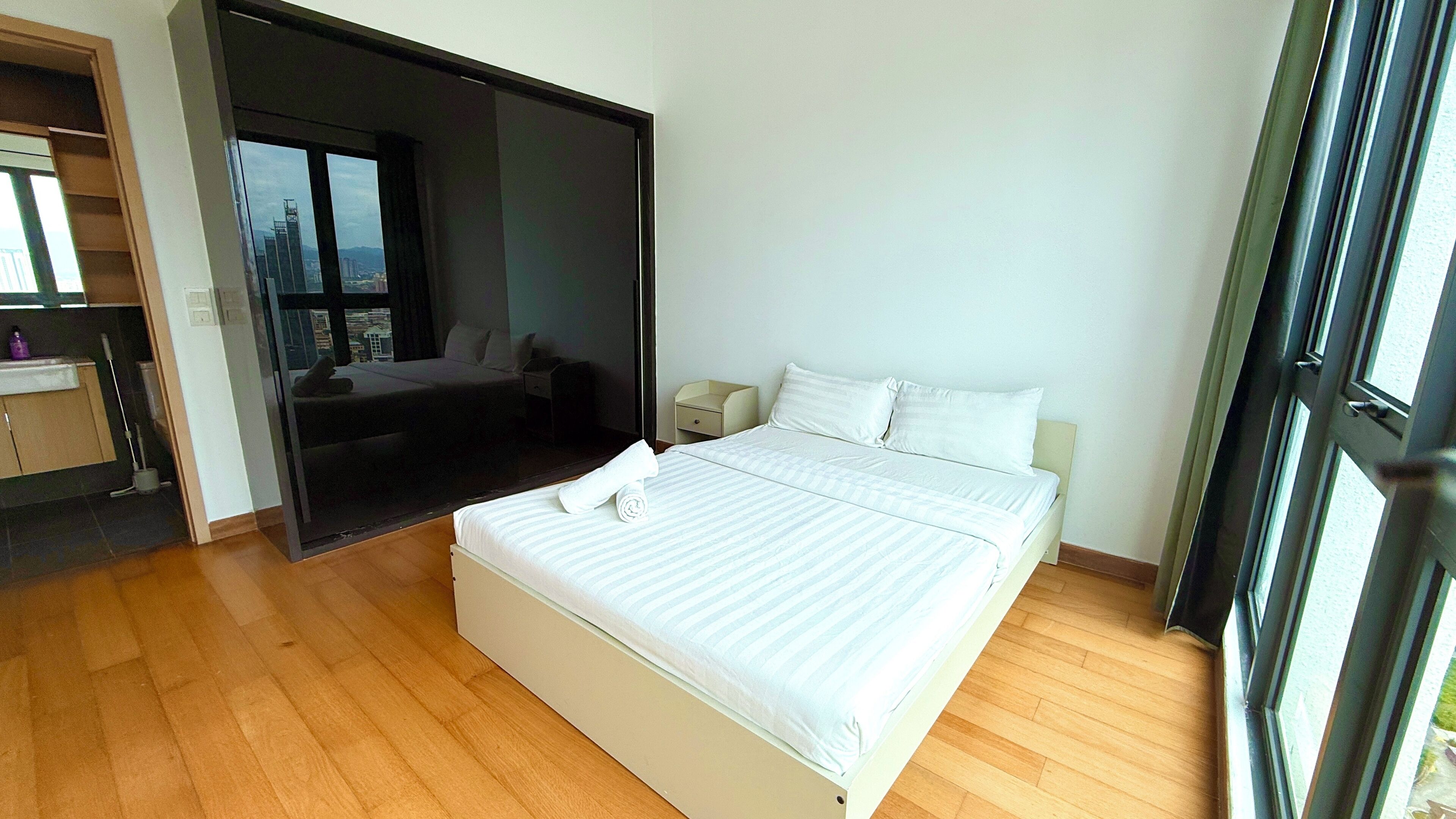 Een slaapkamer met een bed, nachtkastje, raam en uitzicht op een stadsbeeld.