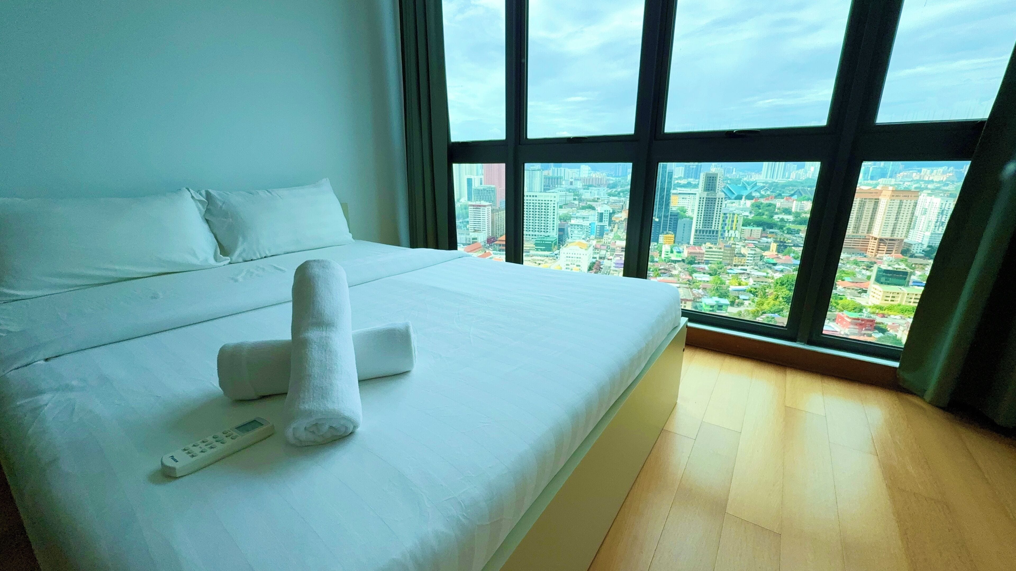 A hotel room with a large bed, a remote control, and a rolled towel.