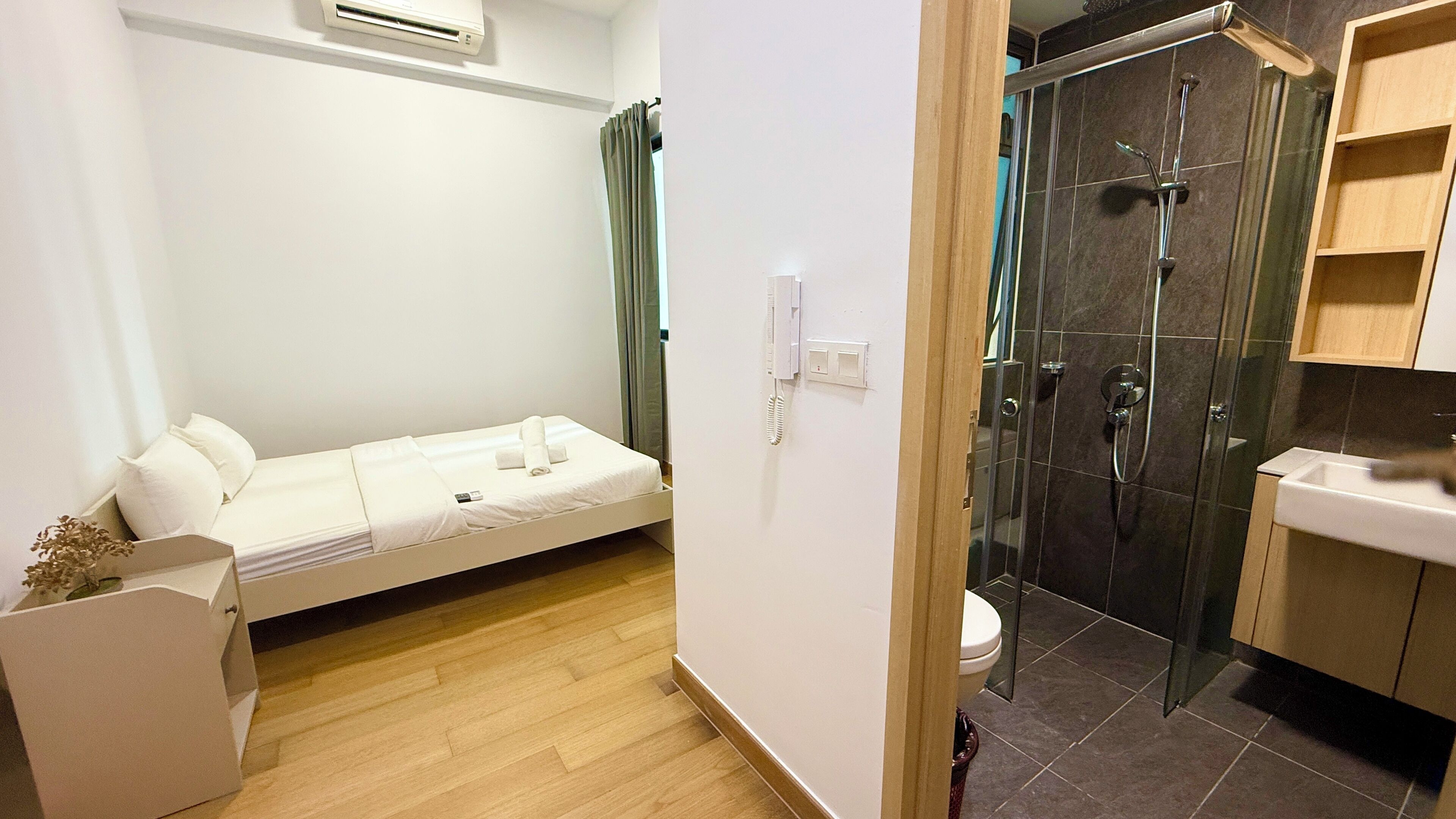 A small, compact room with a bed, a shower, and a sink.