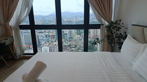 A hotel room with a large window offering a cityscape view, a neatly made bed, and a plant on the side. - The Colony Skyline Suites KLCC (Kuala Lumpur)