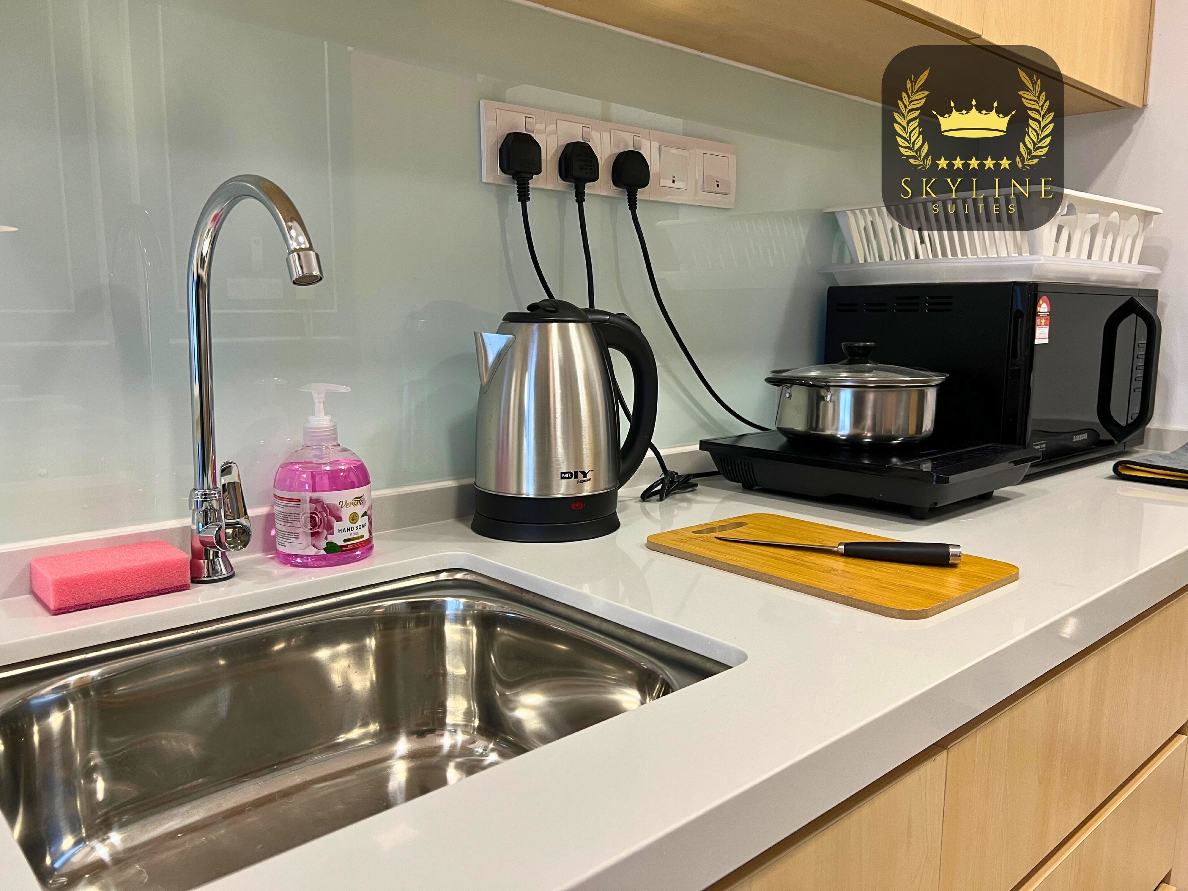 A modern kitchen with a stainless steel sink, a kettle, a microwave, and a cutting board.