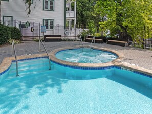 A swimming pool with a tiled edge, a hot tub, and a wooden deck area. - Waterfront Condo, Private Beach, Outdoor Pool & Hot Tub & Walkable to Downtown (Elkhart Lake)