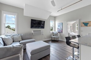 A modern living room with a sectional sofa, a dining area with a table and chairs, and a flat-screen TV mounted on the wall. - Waterfront Condo, Private Beach, Outdoor Pool & Hot Tub & Walkable to Downtown (Elkhart Lake)