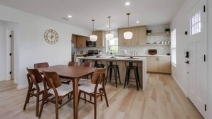 A modern kitchen with wooden cabinets, a central island, pendant lighting, and a dining area with a wooden table and chairs. - Home with views close to all attractions San Diego (Escondido)