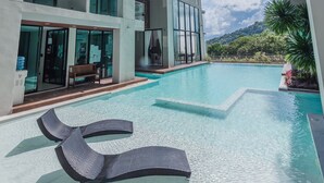 A modern pool area with clear water, lounge chairs, and a view of a mountain. - Condo Viva Patong A401 Freedom Beach (Patong)