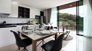 A modern kitchen with a dining area, large windows, and a view of greenery. - Condo Viva Patong A401 Freedom Beach (Patong)