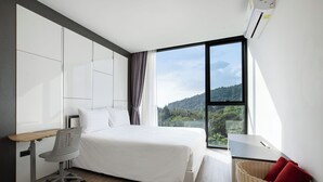A modern hotel room with a large bed, a desk, and a view of a mountainous landscape. - Condo Viva Patong A401 Freedom Beach (Patong)