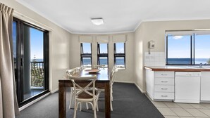 A modern kitchen with a dining area, large windows with ocean views, and a balcony. - Gena Apartments Unit 10 Kings Beach QLD (Kings Beach)