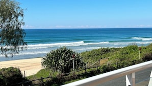 Une route côtière avec vue sur la plage, une barrière de sécurité en métal et un panneau rouge.