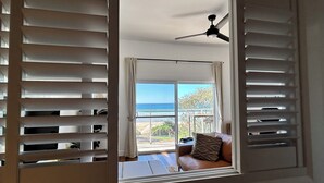 Une chambre avec vue sur l’océan, donnant sur une fenêtre munie de stores.
