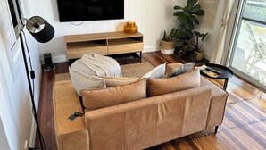 Un salon avec un canapé beige, un téléviseur à écran plat, un plancher en bois et une grande fenêtre donnant sur un beau paysage.